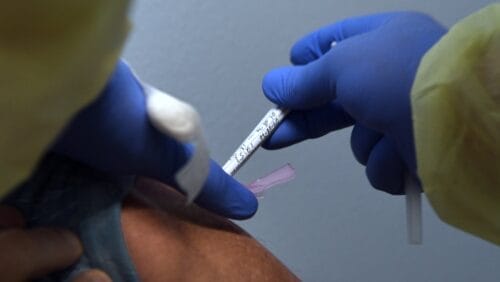 Close framed shot of clinical researcher's gloved hands injecting a patient's arn
