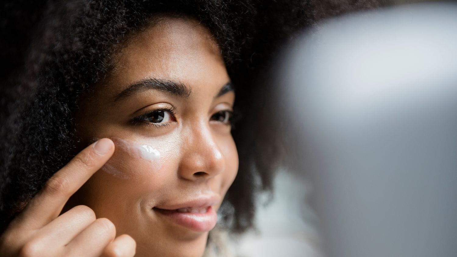 Woman of color putting on tinted sunscreen for dark skin under her eyes