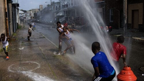 children playing on the streets in a city neighborhood in the summer with the fire hydrant spraying water
